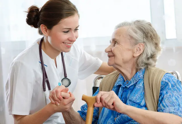 Skilled Nursing A smiling nurse holds hands with an older woman who uses a cane