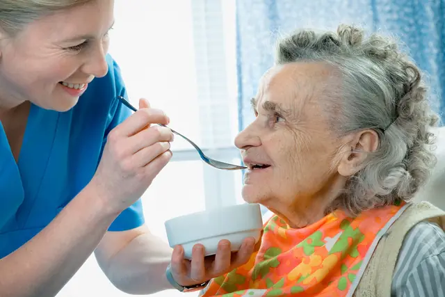 A caregiver helps an older woman eat with a spoon