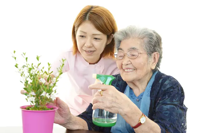 Services A caregiver smiles as an older woman waters a potted plant